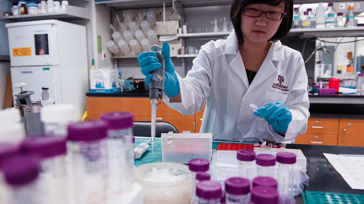 A chemistry researcher at their workstation, holding a pipette