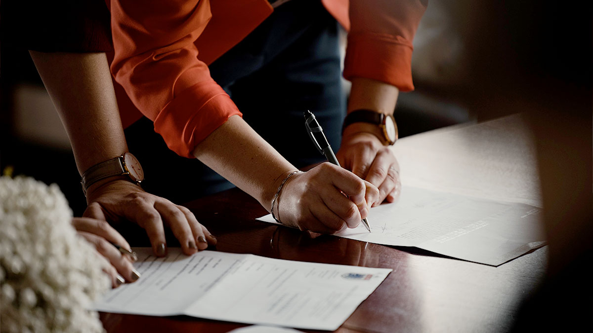 Two people stand next to each other and write on documents