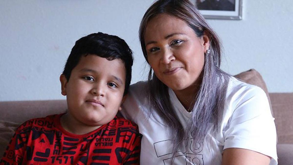 A mother and her son pose for a photo on their couch