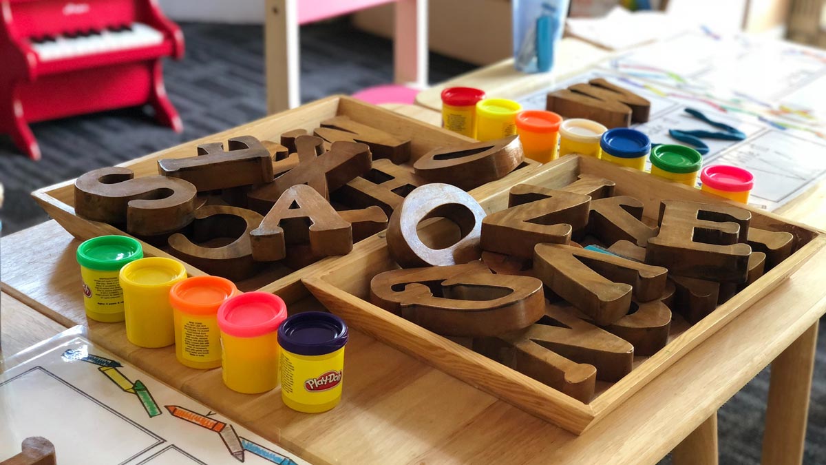 Colorful containers of playdough sit next to a pile of wooden letters